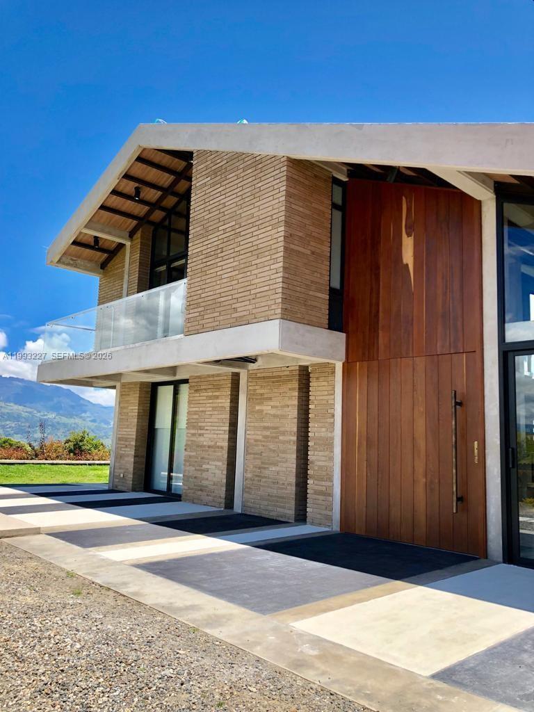 A modern two-story house features brick siding, a large wooden door, and a glass balcony — 4.2 KILOMETRO NW VEREDA BOBADILLAS, Bg, Bg