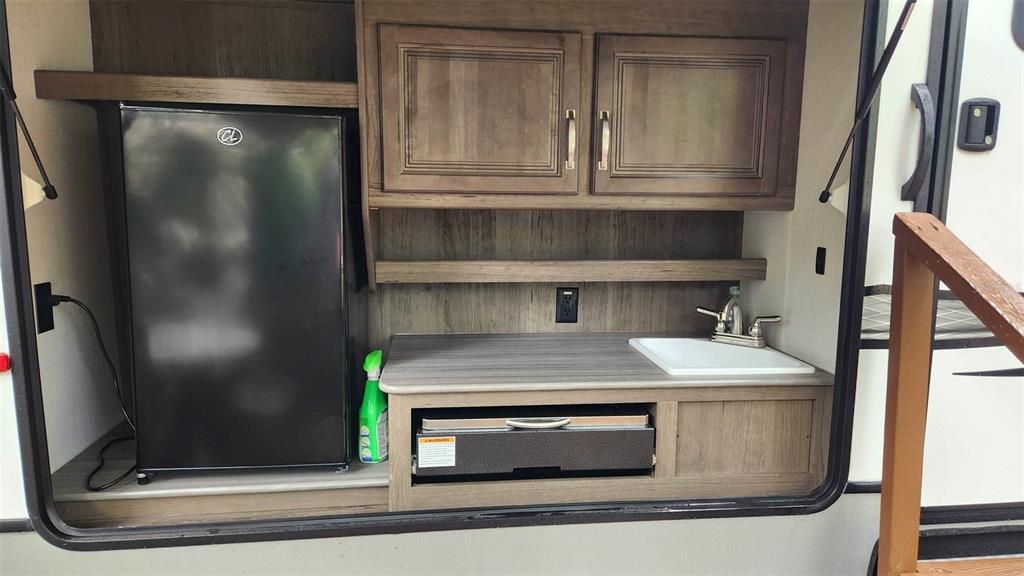 An outdoor kitchen in a recreational vehicle features a mini-fridge, sink, and storage cabinets — 251 SADDLE LANE, LAKE WALES, FL