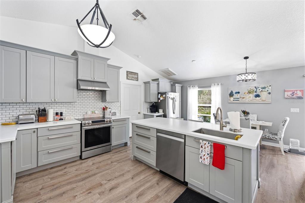 A modern kitchen features gray cabinets, white countertops, stainless steel appliances, and wood-look flooring — 11240 MARQUERITE AVENUE, NEW PORT RICHEY, FL
