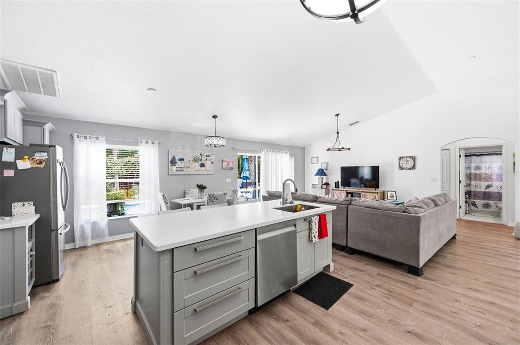 A kitchen island with a stainless steel dishwasher sits before an open-concept living and dining area — 11240 MARQUERITE AVENUE, NEW PORT RICHEY, FL