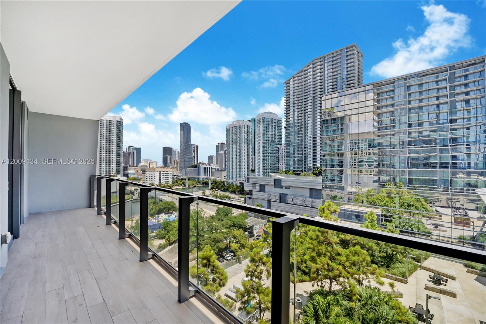 A balcony with glass railings overlooks a city skyline and a green park area — 88 SW 7th St # 1009, Miami FL 33130, MIAMI, FL