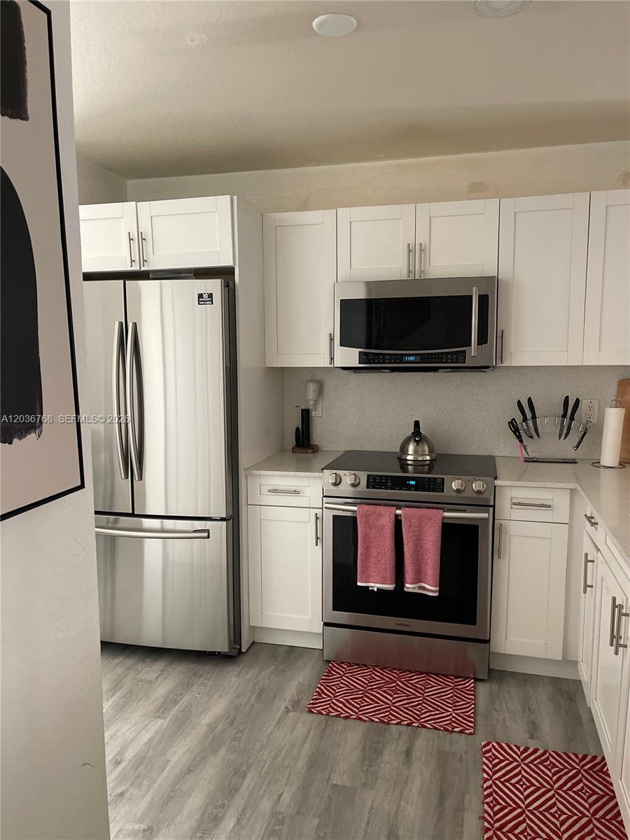 A kitchen features white cabinets, stainless steel appliances, and light wood-look flooring — 2432 SW 99th Way, Miramar FL 33025, MIRAMAR, FL