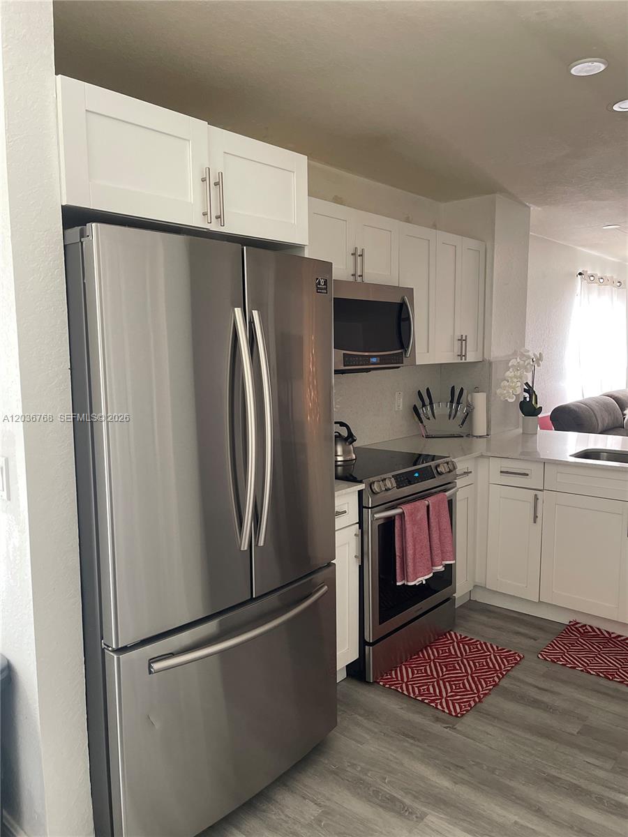 A kitchen features white cabinets, stainless steel appliances, and gray wood-look flooring — 2432 SW 99th Way, Miramar FL 33025, MIRAMAR, FL