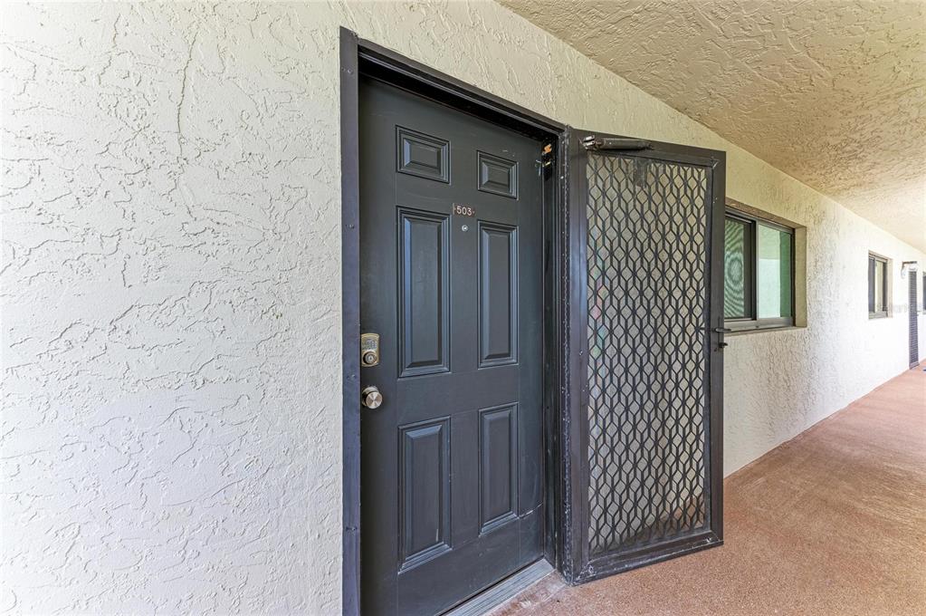 A dark entry door with a security screen door is set in a textured wall — 1510 1ST AVENUE W UNIT 503, BRADENTON, FL