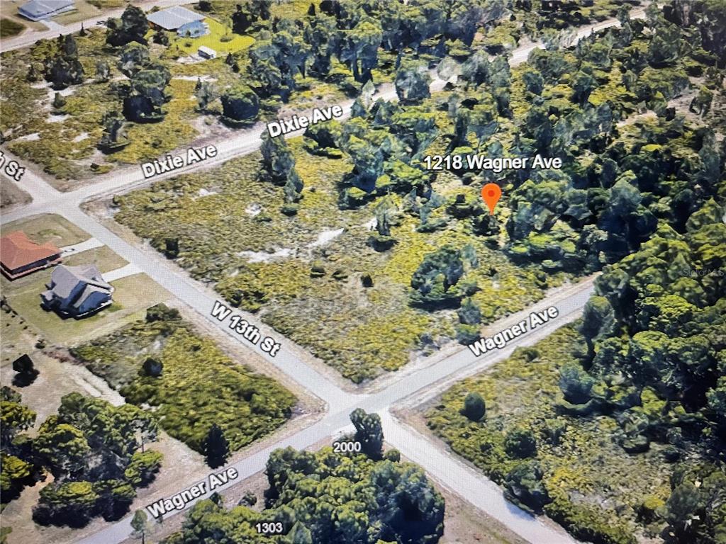 This aerial view shows a wooded, undeveloped corner lot at a residential street intersection — 1218 WAGNER AVENUE, LEHIGH ACRES, FL