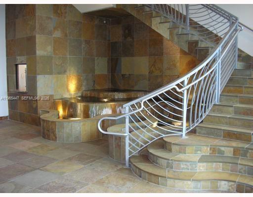 A curved stone staircase with a metal railing sits beside an indoor stone water feature — 1755 E Hallandale Beach Blvd # 406E, Hallandale Beach FL 33009, HALLANDALE BEACH, FL