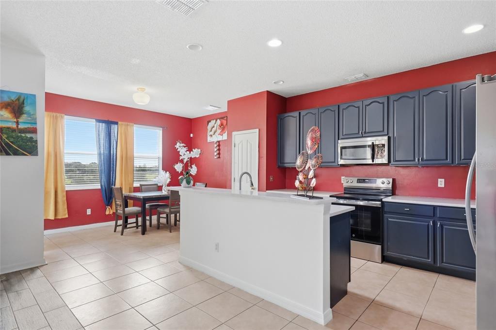 A kitchen with dark blue cabinets, red walls, and a white island faces a dining area — 7254 COUNTRY RUN PARKWAY, ORLANDO, FL