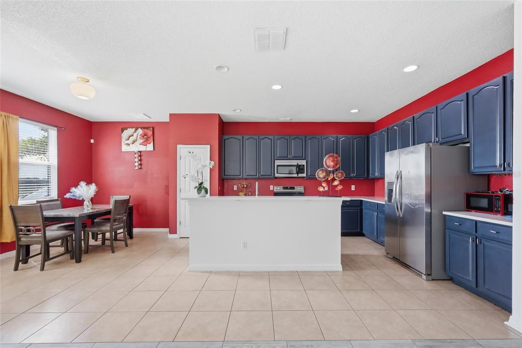 A kitchen with blue cabinets, a white island, and red walls, adjacent to a dining area — 7254 COUNTRY RUN PARKWAY, ORLANDO, FL