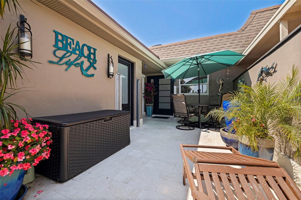 A paved patio features a storage bin, outdoor furniture, a green umbrella, and potted plants — 479 BOCA CIEGA POINT BOULEVARD S UNIT 1205, ST PETERSBURG, FL