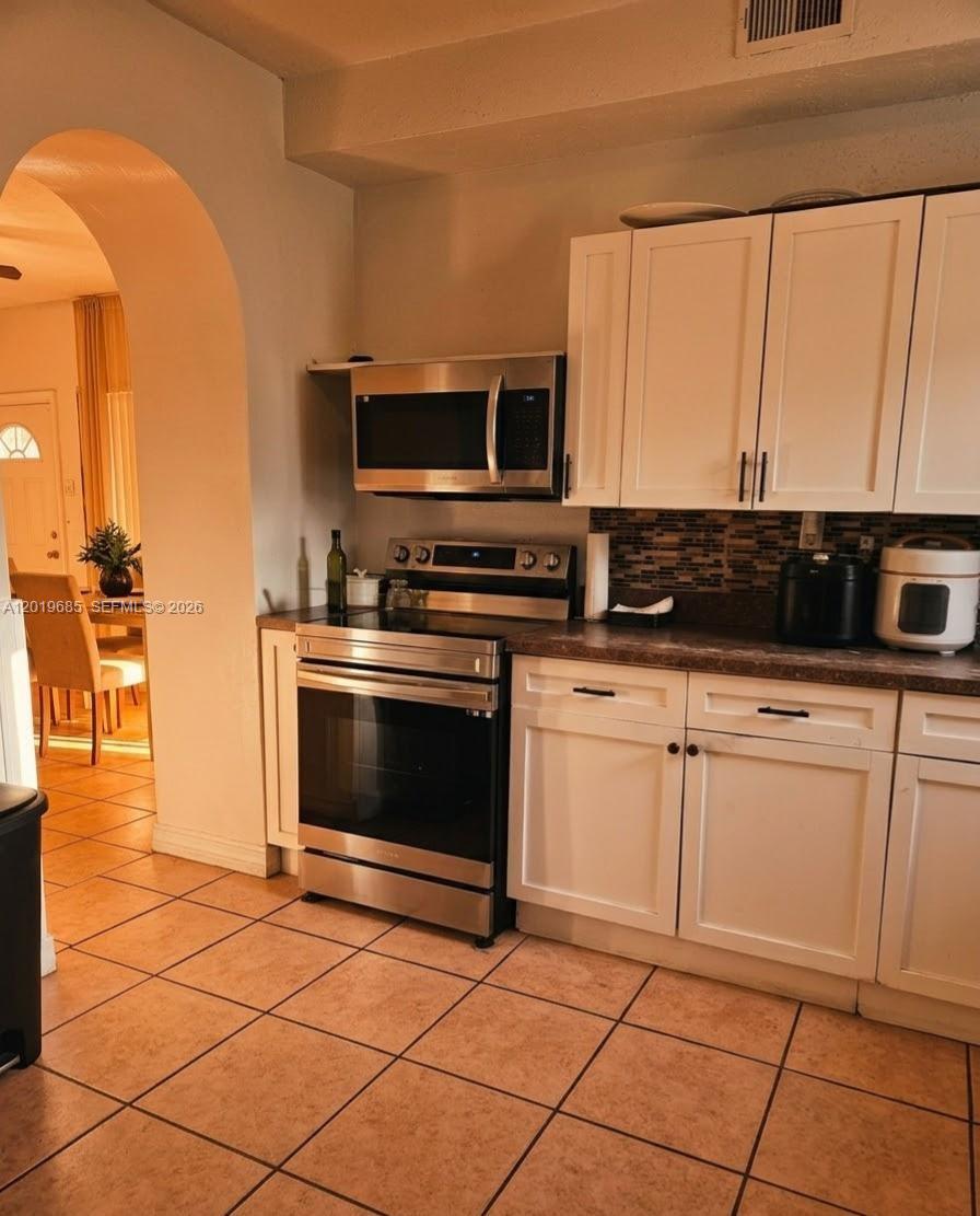 A kitchen features white cabinets, stainless steel appliances, and a tiled floor — 571 NE 172nd St, North Miami Beach FL 33162, NORTH MIAMI BEACH, FL