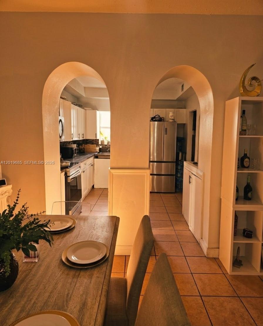 A dining area with a wooden table leads through two arched openings into a kitchen — 571 NE 172nd St, North Miami Beach FL 33162, NORTH MIAMI BEACH, FL