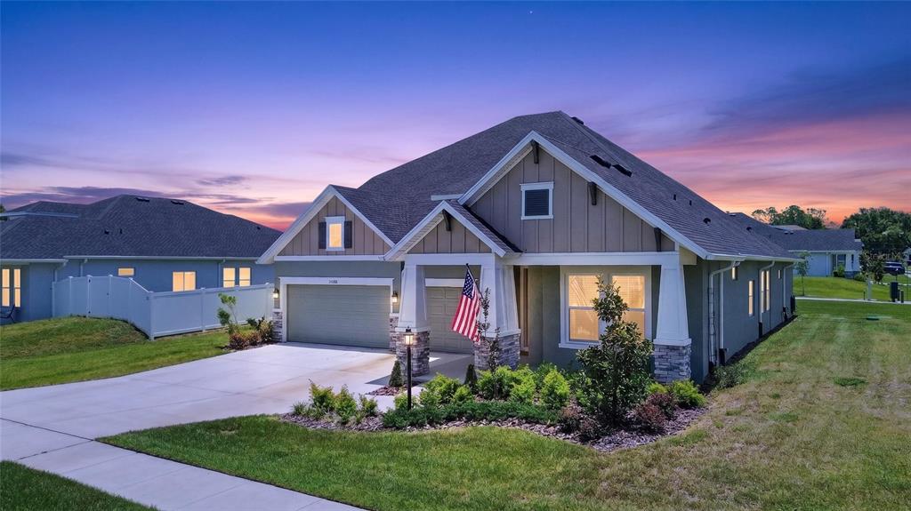 A single-story house with a two-car garage, stone accents, and an American flag at dusk — 12862 CARMELA CIRCLE W, SAN ANTONIO, FL