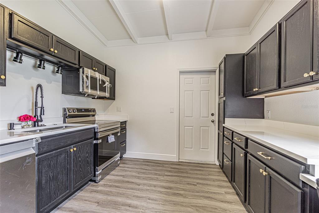 A kitchen features dark wood cabinets, stainless steel appliances, white countertops, and wood-look flooring — 416 COUNTRY CLUB DRIVE, OLDSMAR, FL