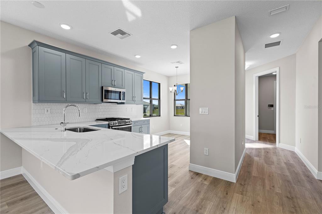A modern kitchen features blue cabinets, white quartz countertops, and light wood-look flooring — 18388 ROCKPORT PLACE, LAKEWOOD RANCH, FL