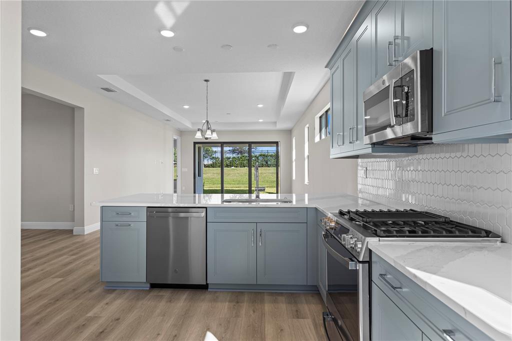 A kitchen features blue cabinets, stainless steel appliances, white countertops, and light wood-look flooring — 18388 ROCKPORT PLACE, LAKEWOOD RANCH, FL