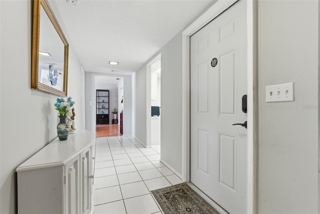 A bright entryway features white tile flooring, light gray walls, and a white front door — 1141 MERLE WAY UNIT 14, SARASOTA, FL