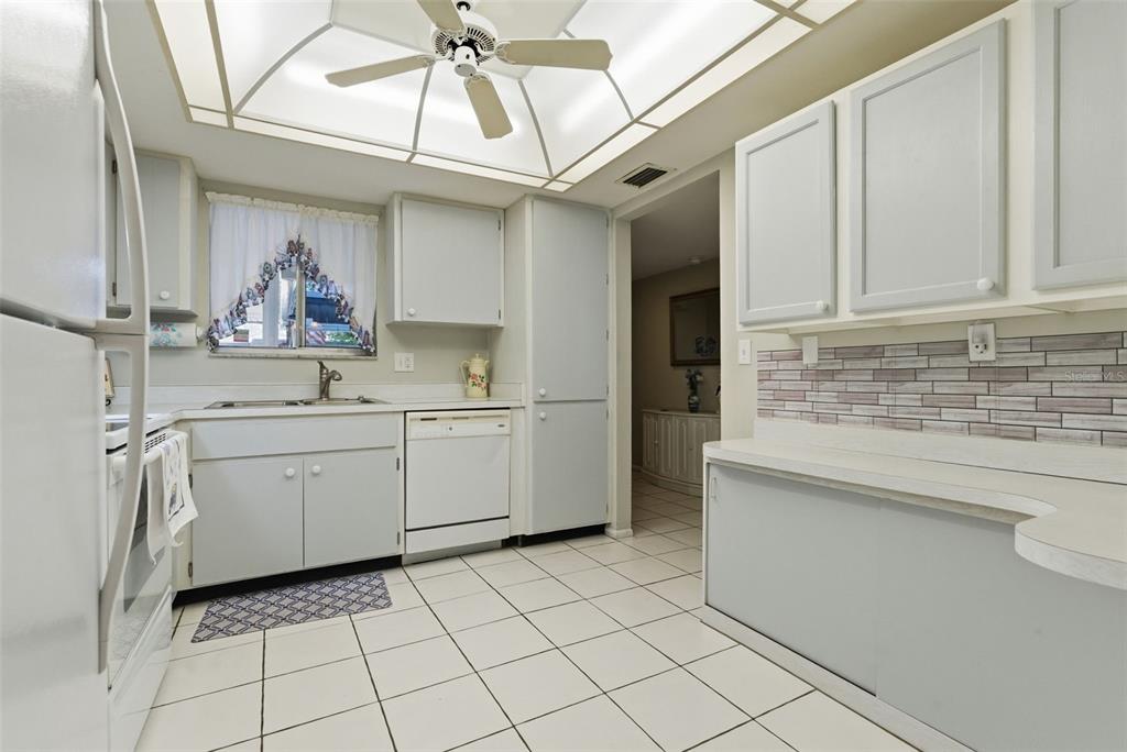 A kitchen features light gray cabinets, white appliances, a tiled backsplash, and a ceiling fan — 1141 MERLE WAY UNIT 14, SARASOTA, FL