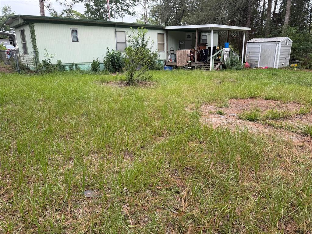 A light green mobile home with a covered porch and a small shed in the yard — 6363 REED DRIVE, KEYSTONE HEIGHTS, FL