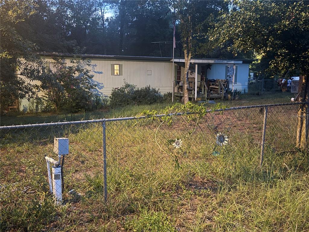 A single-story mobile home sits behind a chain-link fence in a grassy, wooded yard — 6363 REED DRIVE, KEYSTONE HEIGHTS, FL