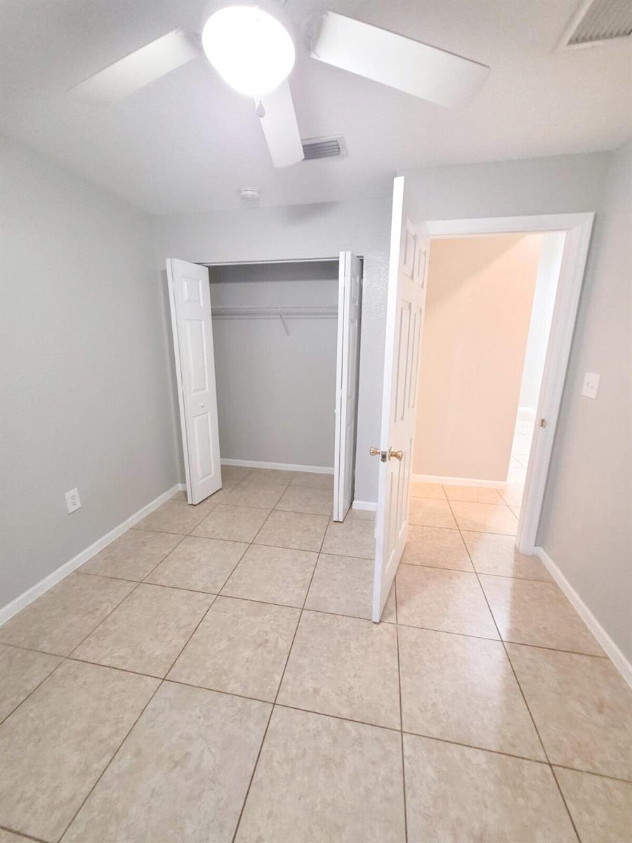 A bedroom with light gray walls, tile flooring, a ceiling fan, and an open closet — 524 Southridge Road, Delray Beach FL 33444, DELRAY BEACH, FL