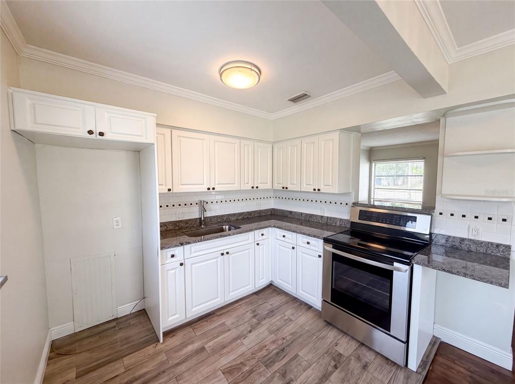 A kitchen features white cabinets, granite countertops, a stainless steel stove, and wood-look flooring — 6129 5TH AVENUE N, ST PETERSBURG, FL