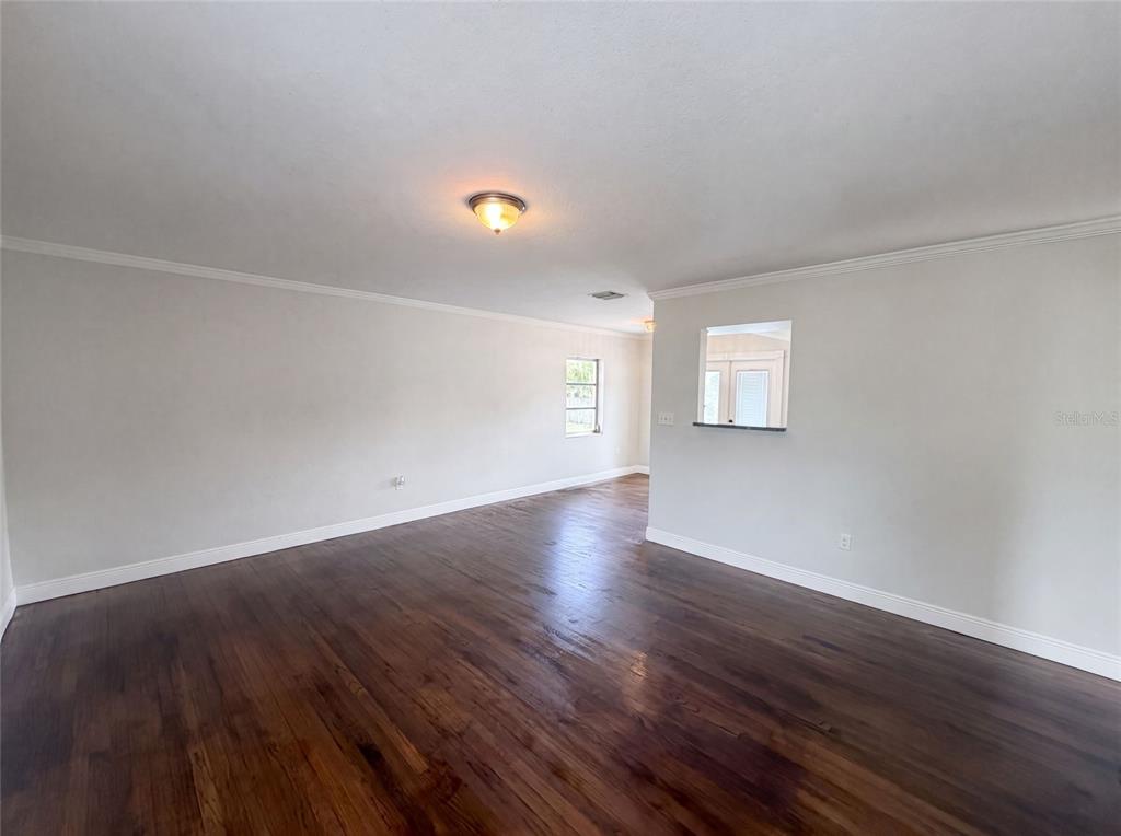An empty living room features dark hardwood floors, white walls, and a pass-through window — 6129 5TH AVENUE N, ST PETERSBURG, FL
