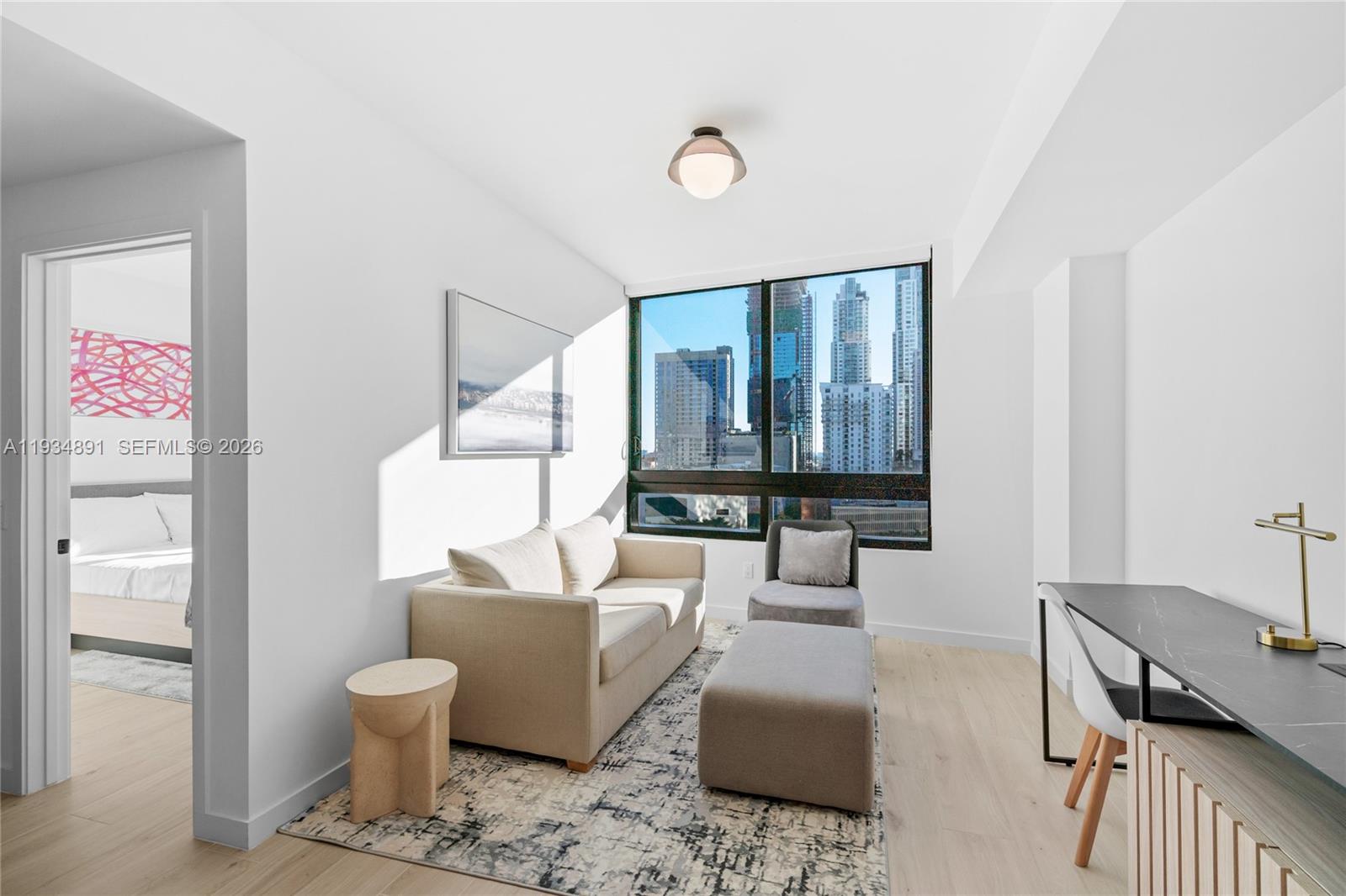 A modern living room features a beige sofa, a desk, and large windows with city views — 225 N Miami Ave # 1405, Miami FL 33132, MIAMI, FL