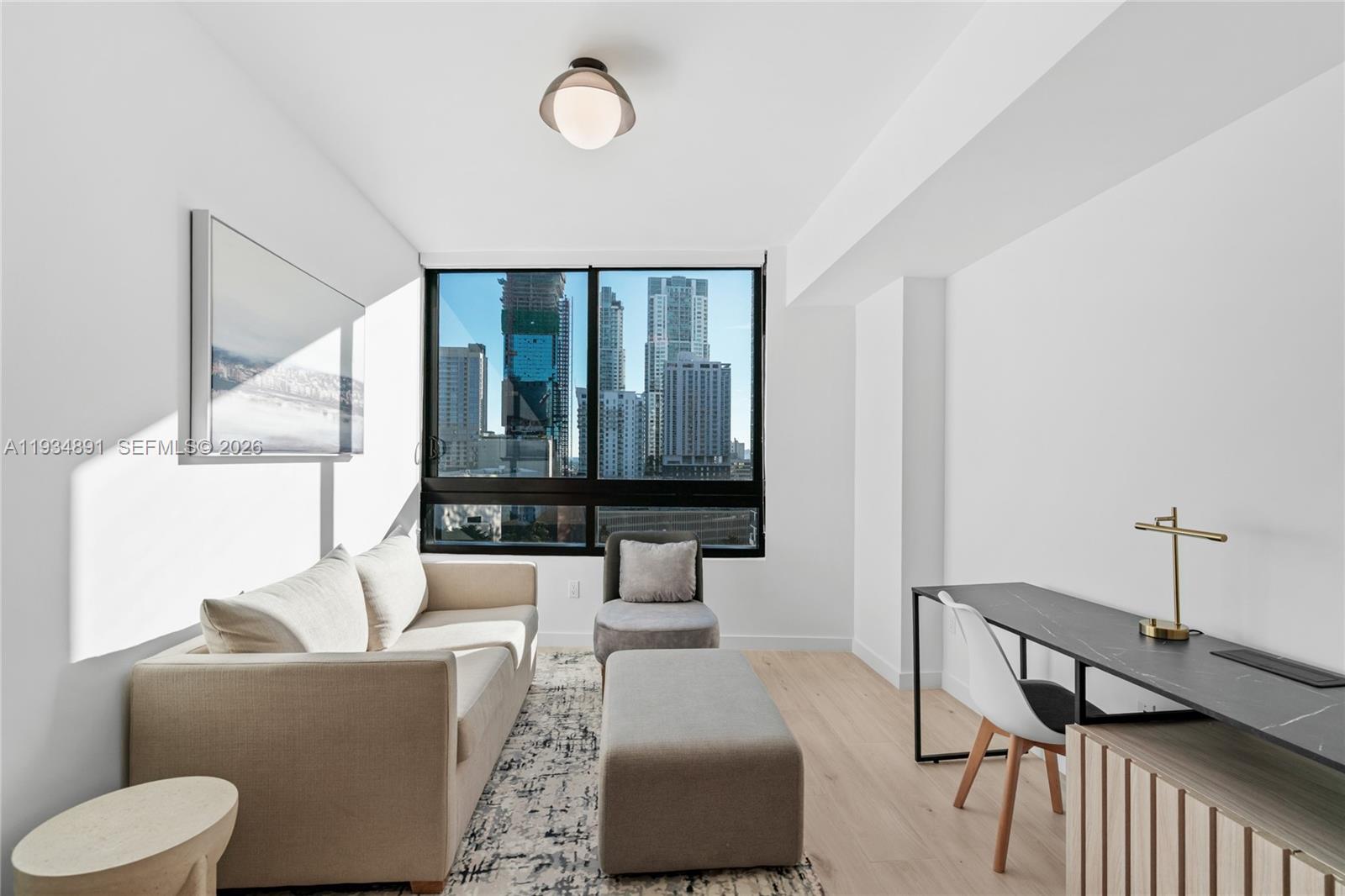 A modern living room features a beige sofa, a desk, and a city skyline view — 225 N Miami Ave # 1405, Miami FL 33132, MIAMI, FL