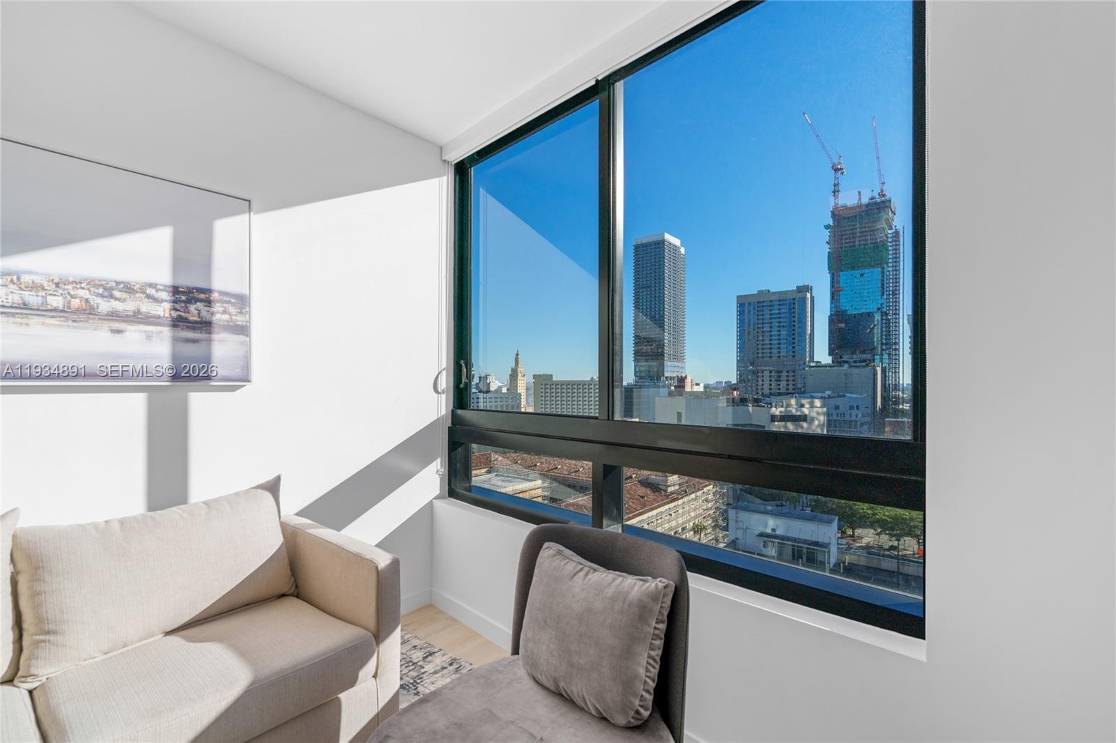 A room with a sofa and chair features a large window overlooking a city skyline — 225 N Miami Ave # 1405, Miami FL 33132, MIAMI, FL