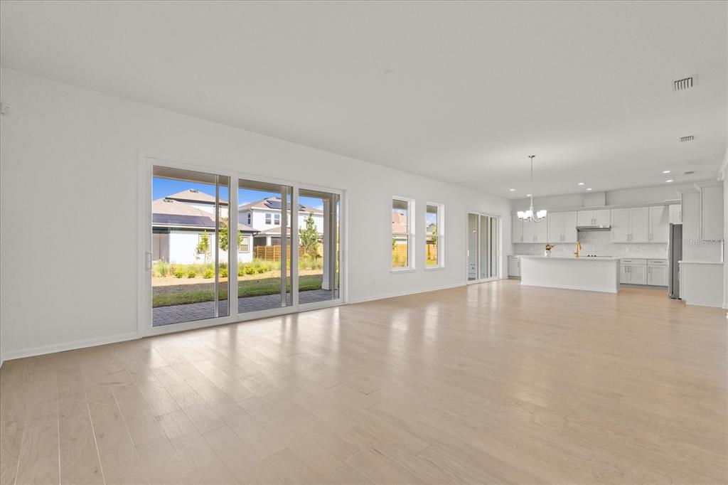 A spacious, open-concept living area with light wood floors, white walls, and a modern kitchen — 3113 EXPEDITION DRIVE, ST CLOUD, FL