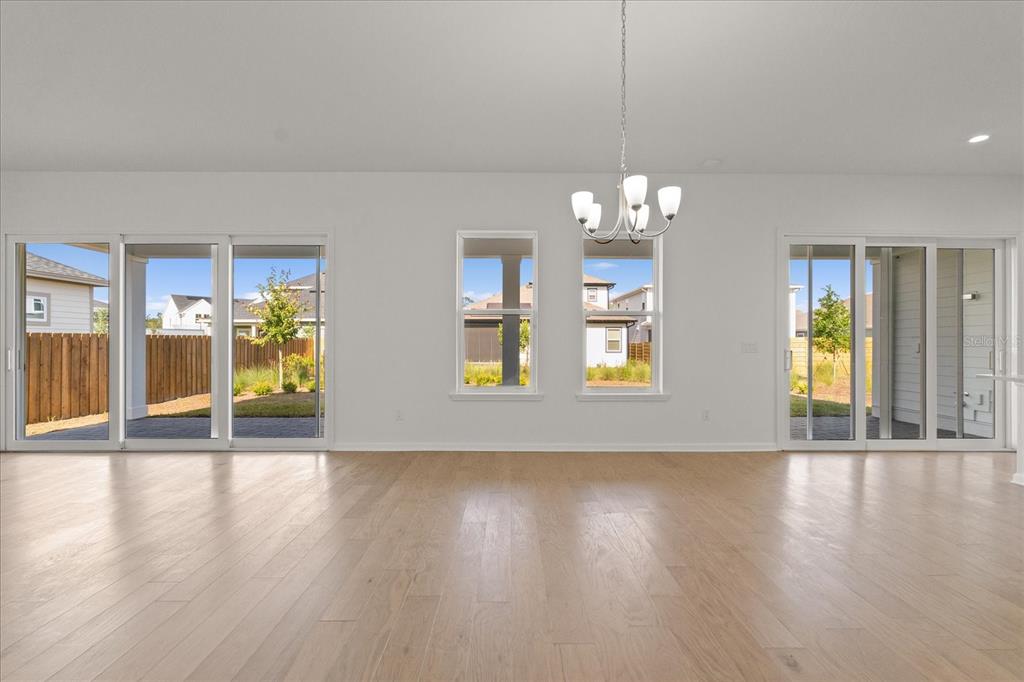 An empty room with light wood flooring, a chandelier, and large sliding glass doors — 3113 EXPEDITION DRIVE, ST CLOUD, FL