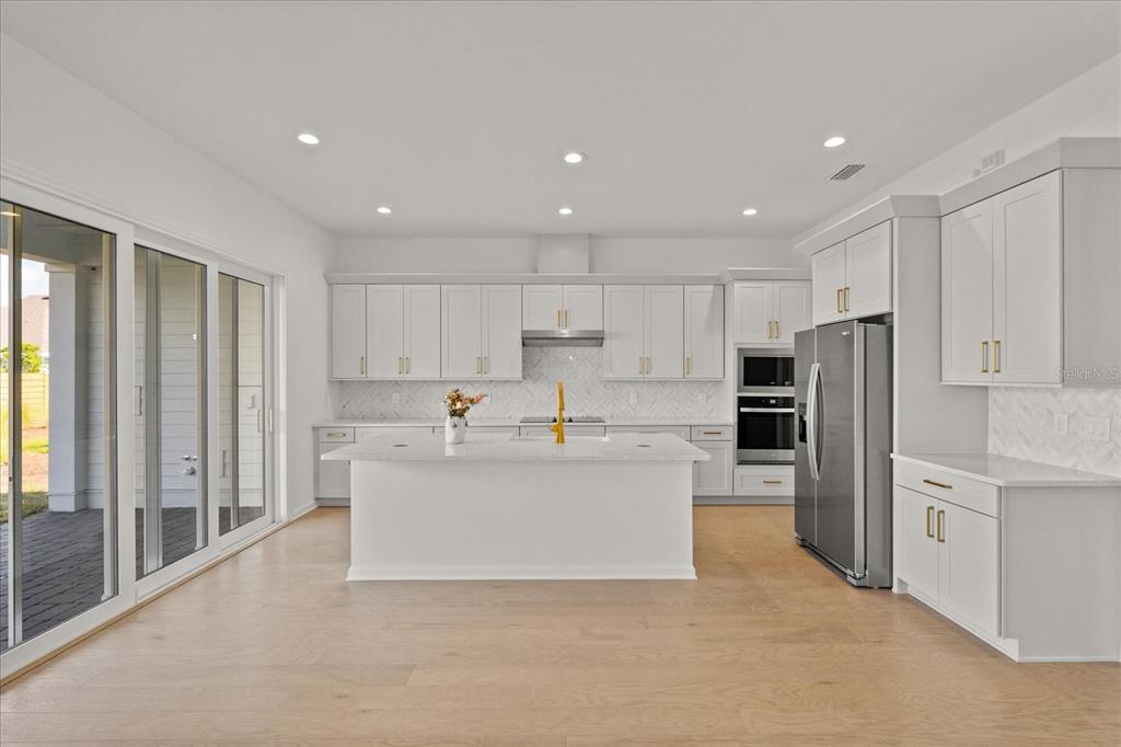 A modern kitchen features white cabinetry, a central island, stainless appliances, and light wood flooring — 3113 EXPEDITION DRIVE, ST CLOUD, FL