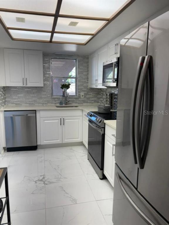A kitchen with white cabinets, stainless steel appliances, a tiled backsplash, and marble-look floor tiles — 9700 STARKEY ROAD UNIT 113, SEMINOLE, FL