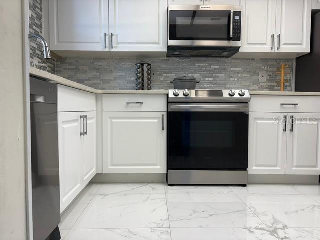 A kitchen features white cabinets, stainless steel appliances, and a tiled backsplash — 9700 STARKEY ROAD UNIT 113, SEMINOLE, FL