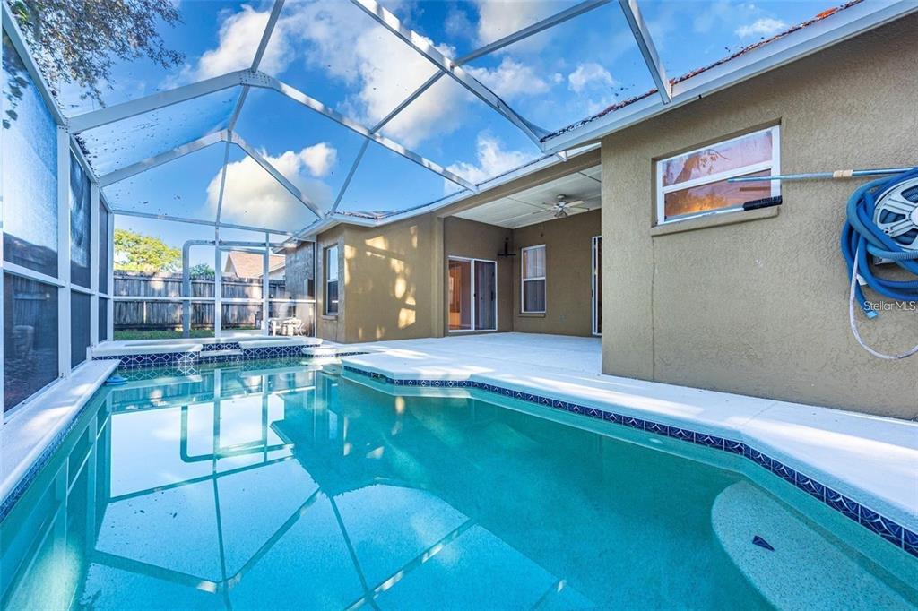 A swimming pool with a screened enclosure sits beside a tan house with a patio — 2634 BROOKVILLE DRIVE, VALRICO, FL
