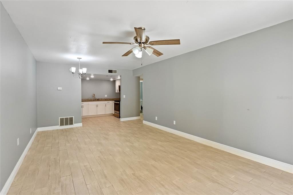 A living room with light wood-look tile flooring, gray walls, and an open kitchen area — 7614 NACIDO COURT UNIT 7614, TAMPA, FL