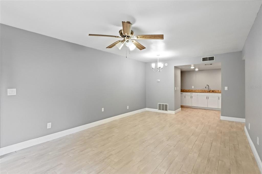 A living area with light wood-look tile flooring, gray walls, and an adjacent wet bar — 7614 NACIDO COURT UNIT 7614, TAMPA, FL