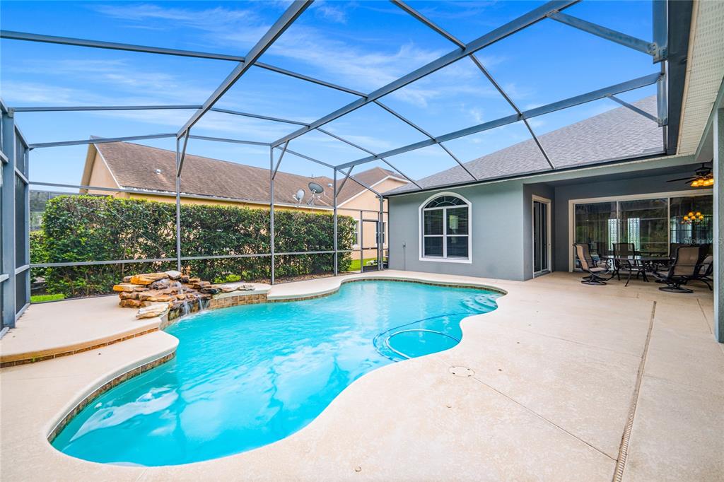 A screened-in patio features a freeform swimming pool with a rock waterfall and concrete decking — 5977 LAKE MELROSE DRIVE, ORLANDO, FL