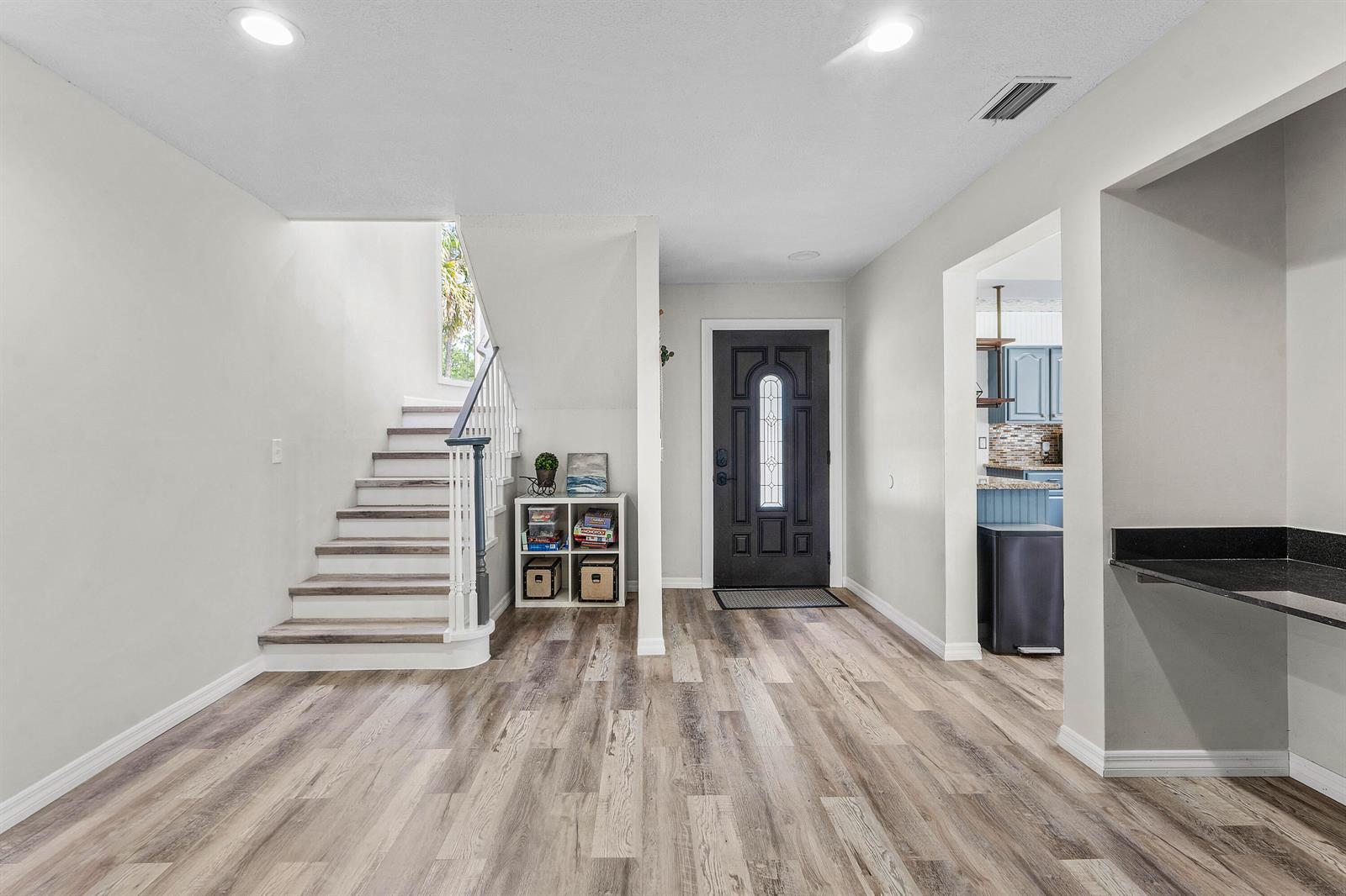 An entryway features wood-look flooring, a staircase with white railings, and a dark front door — 9743 169th Court N, Jupiter FL 33478, JUPITER, FL