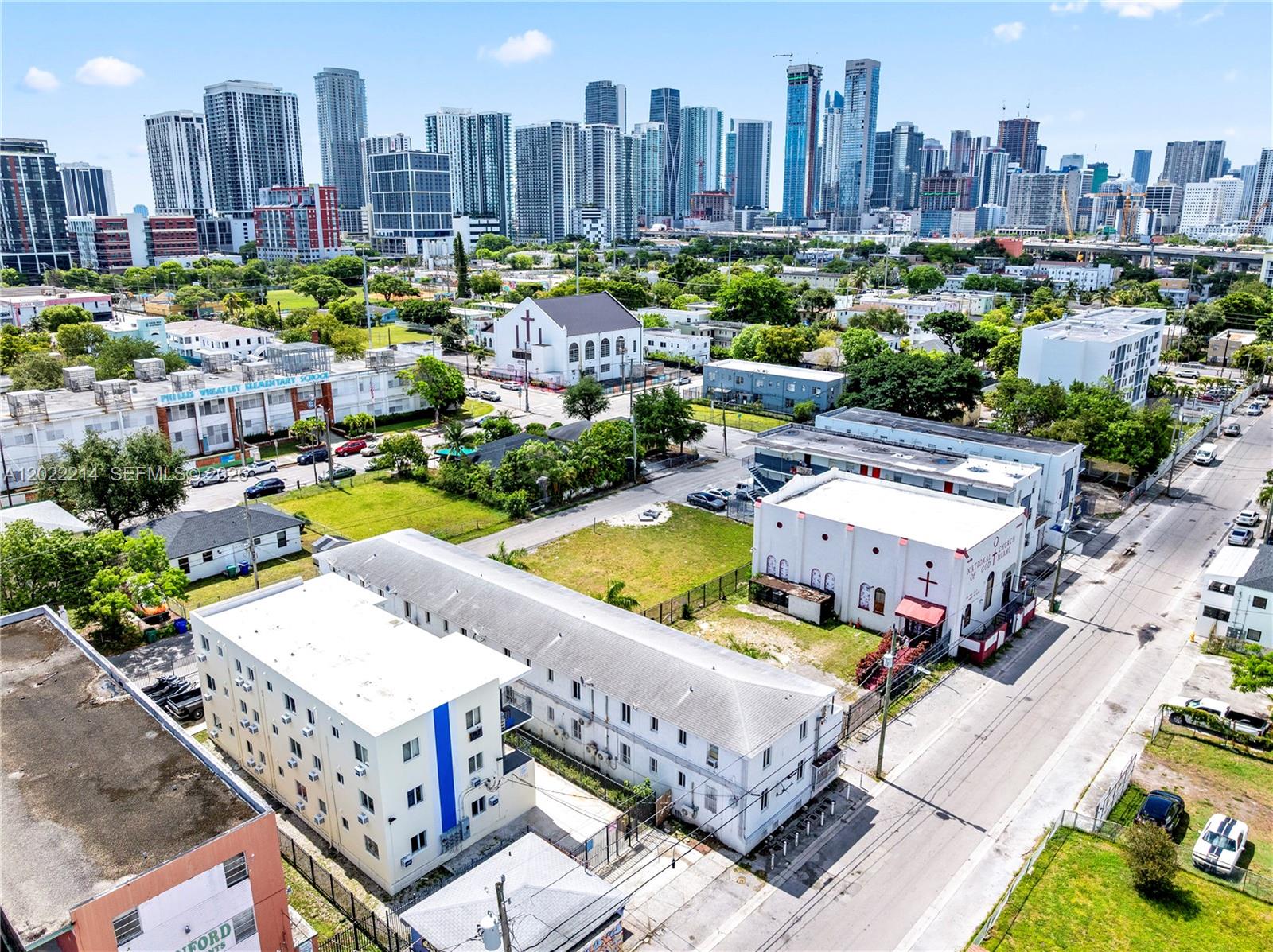 An aerial view shows a city neighborhood with low-rise buildings, churches, and a distant skyline — 1829 NW 2nd Ct, Miami FL 33136, MIAMI, FL