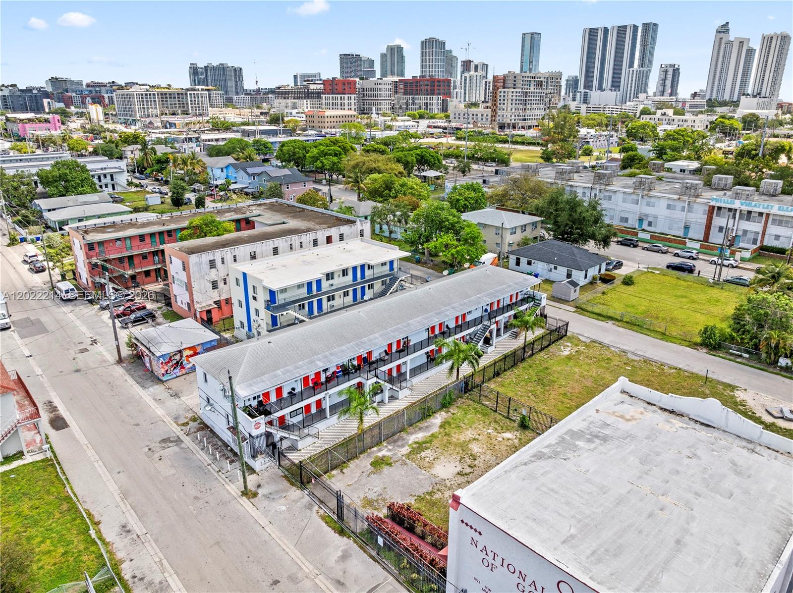 An aerial view shows multi-story apartment buildings with red and blue accents near a city skyline — 1829 NW 2nd Ct, Miami FL 33136, MIAMI, FL