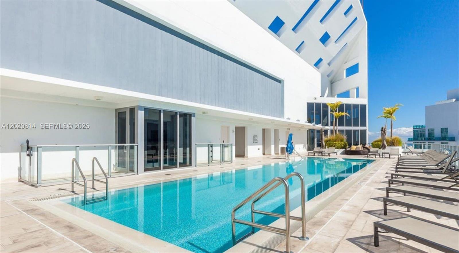 A rectangular swimming pool sits on a terrace next to a modern white building — 1300 Brickell Bay Dr # 1805, Miami FL 33131, MIAMI, FL