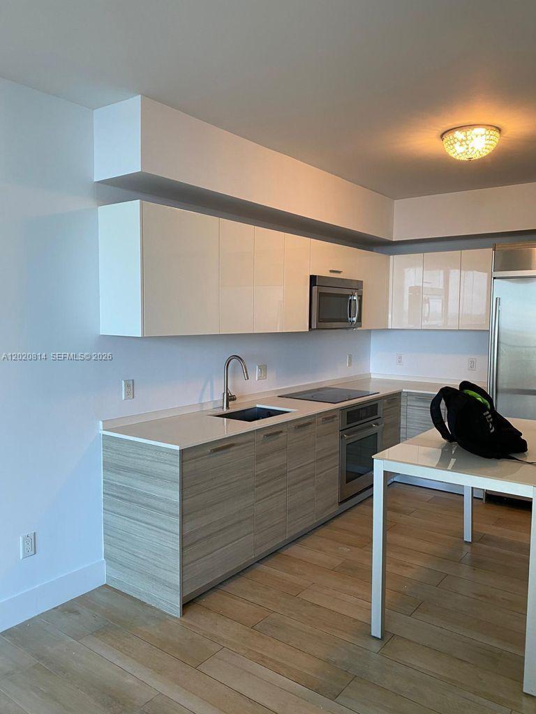 A modern kitchen features white upper cabinets, wood-grain lower cabinets, and stainless steel appliances — 1300 Brickell Bay Dr # 1805, Miami FL 33131, MIAMI, FL