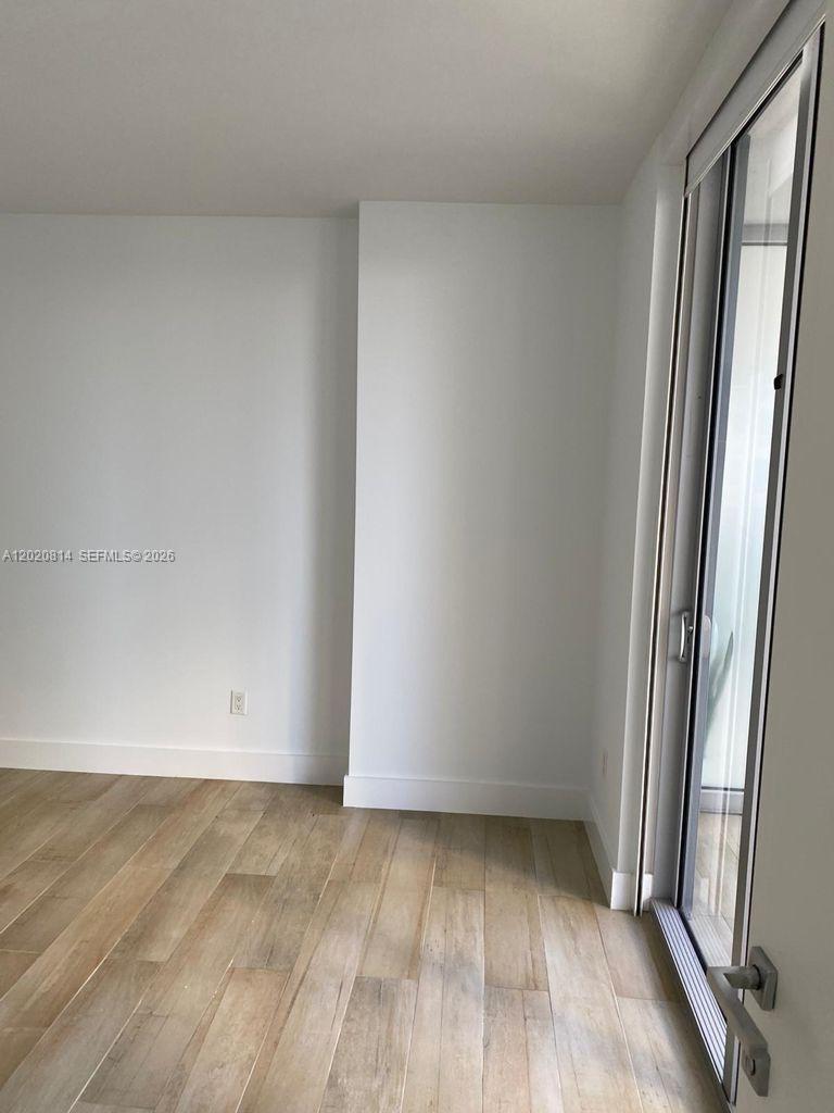 An empty room features light wood-look flooring, white walls, and a sliding glass door — 1300 Brickell Bay Dr # 1805, Miami FL 33131, MIAMI, FL