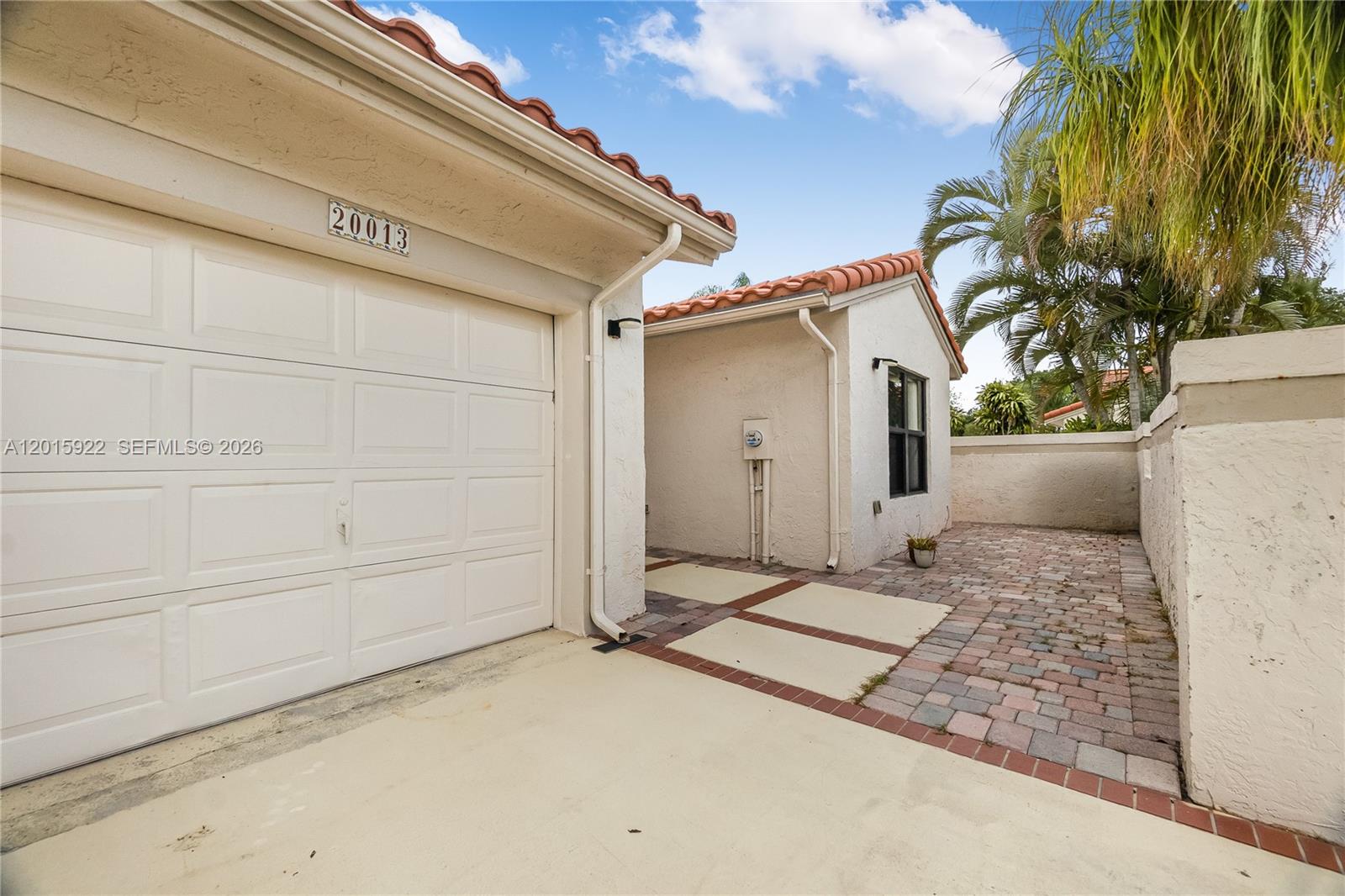 A white stucco house exterior features a garage, a tiled roof, and a paved courtyard — 20013 Mona Cir, Boca Raton FL 33434, BOCA RATON, FL