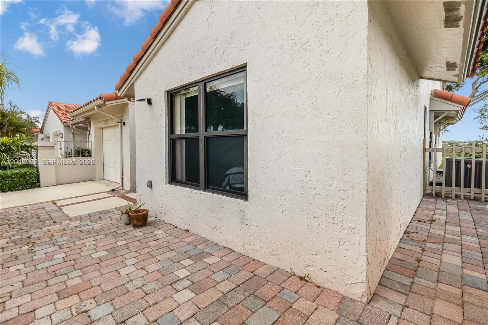 A paved patio sits beside the stucco exterior wall of a house with a window — 20013 Mona Cir, Boca Raton FL 33434, BOCA RATON, FL