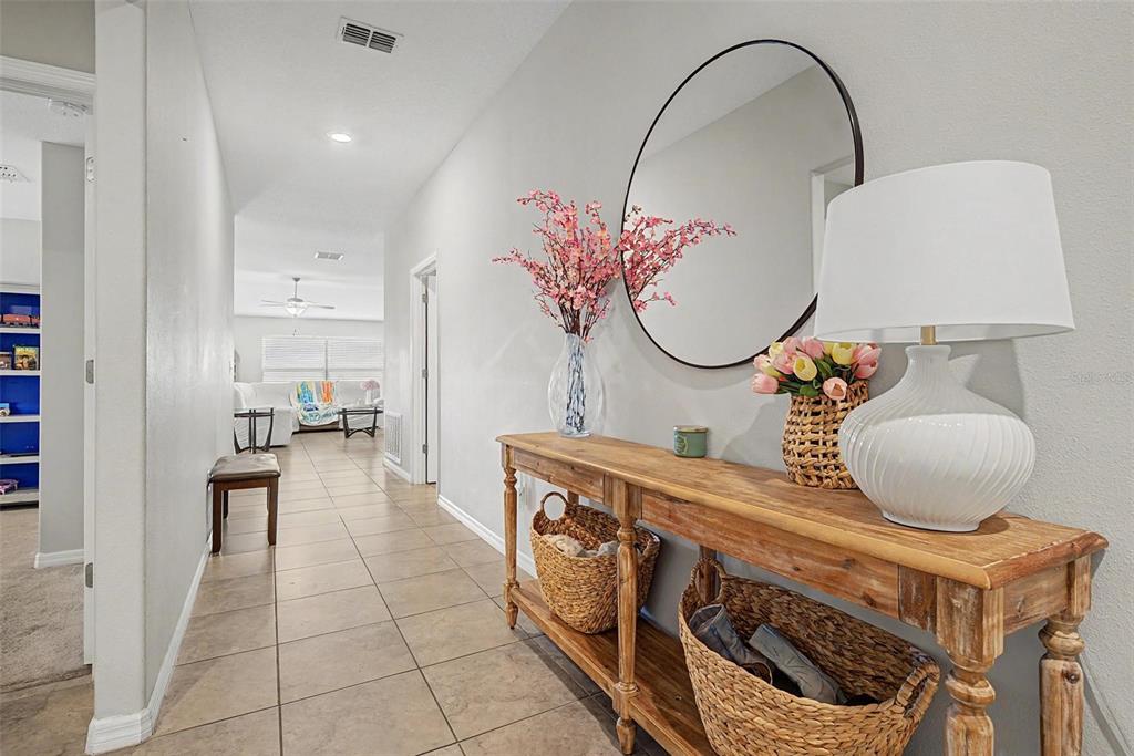 A hallway features a wooden console table with baskets, a round mirror, and tile flooring — 9625 SAGE CREEK DRIVE, RUSKIN, FL