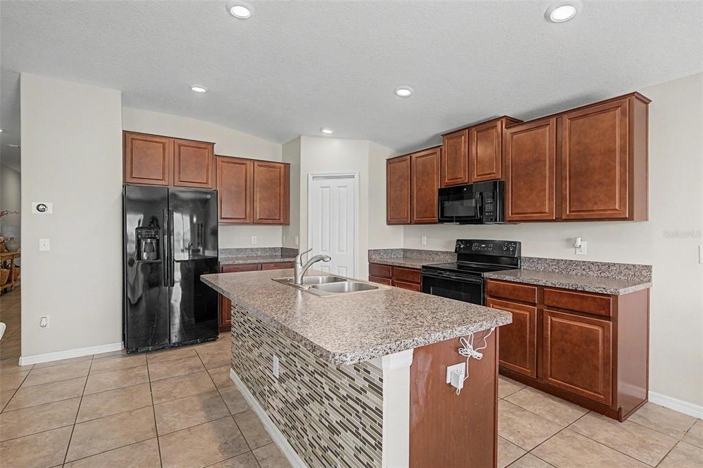 A kitchen features brown wooden cabinets, granite countertops, a central island, and black appliances — 9625 SAGE CREEK DRIVE, RUSKIN, FL