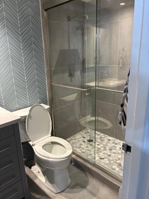 A bathroom features a toilet next to a glass-enclosed shower with pebble flooring and gray tiles — 195 Monaco E, Delray Beach FL 33446, DELRAY BEACH, FL