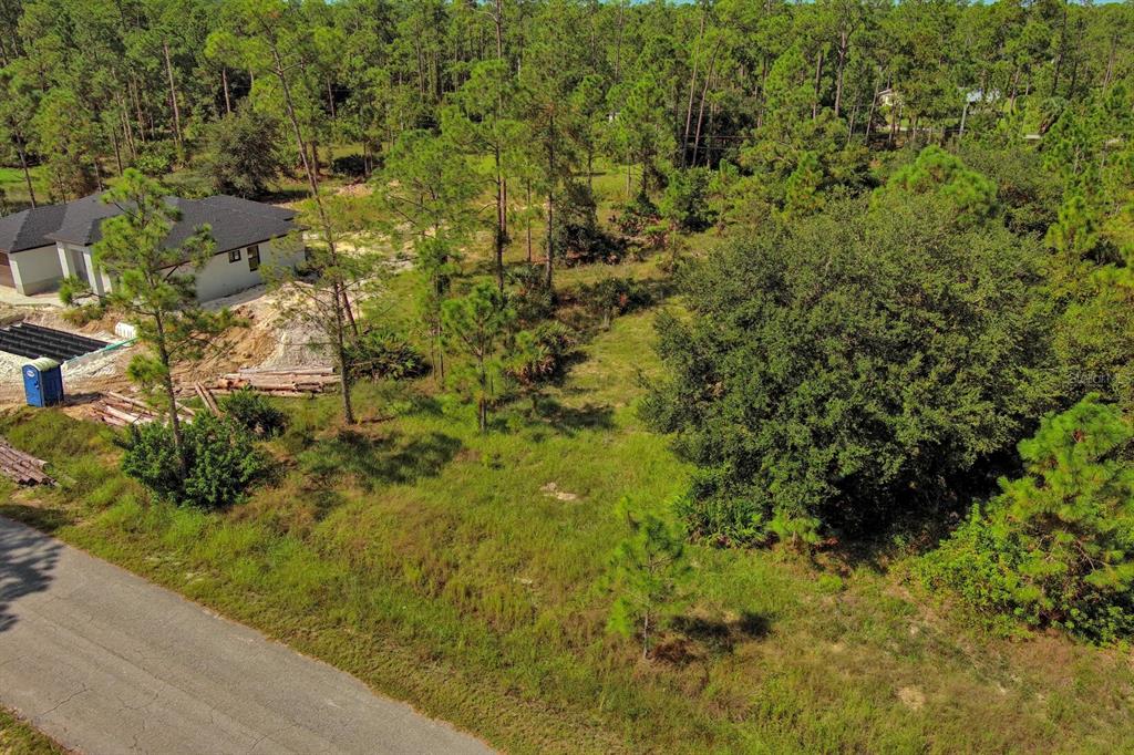 An aerial view shows a vacant, grassy lot with trees next to a house under construction — 1219 WASHINGTON AVENUE, LEHIGH ACRES, FL